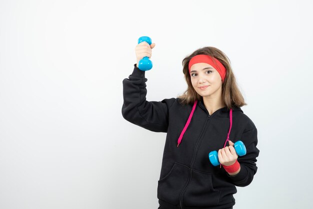 Young sporty woman standing and holding blue dumbbells. High quality photo