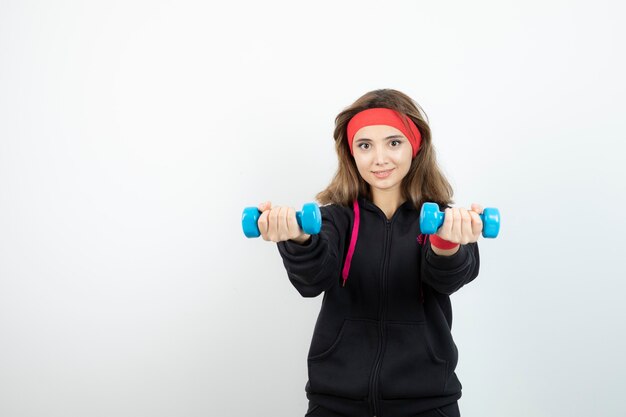 Young sporty woman standing and holding blue dumbbells. 