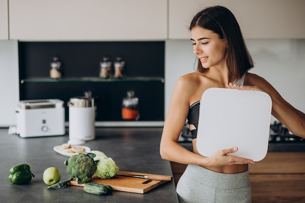 Young sporty woman with scales at kitchen