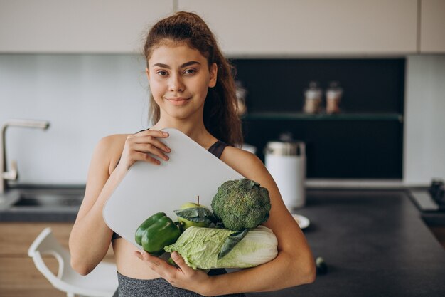 Молодая спортивная женщина с весами и овощами на кухне