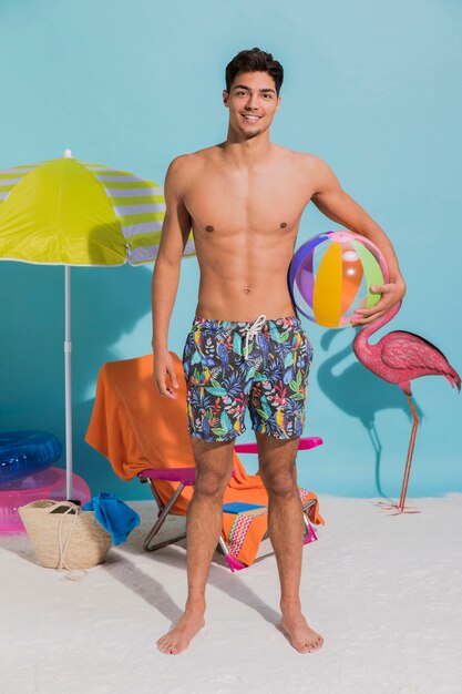 Young standing man in swimwear holding inflatable ball