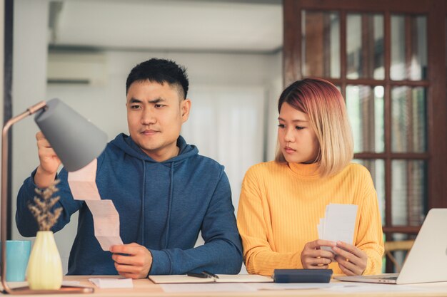 Young stressed asian couple managing finances, reviewing their bank accounts using laptop computer 