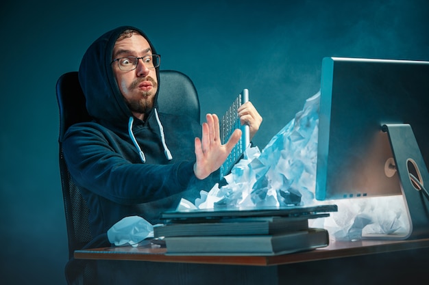 Free photo young stressed handsome businessman working at desk in modern office shouting at laptop screen and being angry about spam