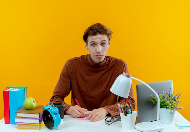 Foto gratuita ragazzo giovane studente seduto alla scrivania con strumenti di scuola scrivendo qualcosa