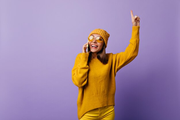 Young student generated new idea by talking on phone. Joyful from her discovering, girl in yellow clothes inspired posing on lilac