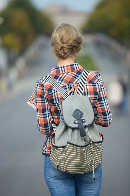 Foto gratuita giovane ragazza studente che cammina lungo la strada con uno zaino