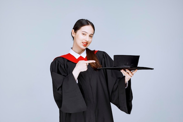 Young student in gown pointing at cap. High quality photo