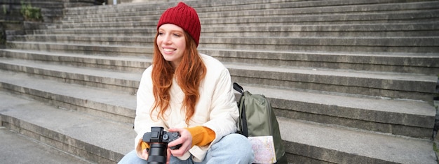 Foto gratuita la giovane fotografa studentessa si siede sulle scale della strada e controlla i suoi scatti durante la ripresa di una fotocamera professionale