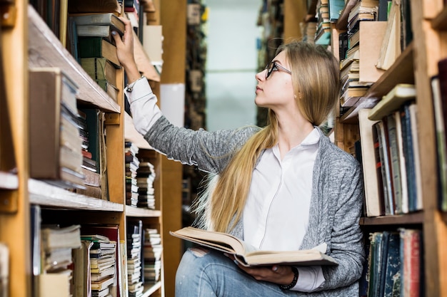 Free photo young student picking books from bookshelf