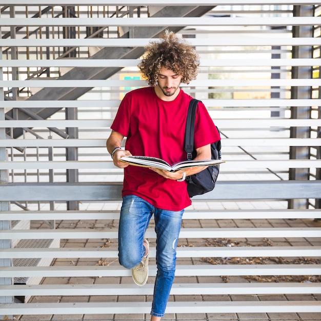 Young student reading book near wall