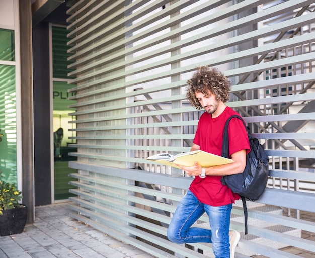 Young student reading near wall