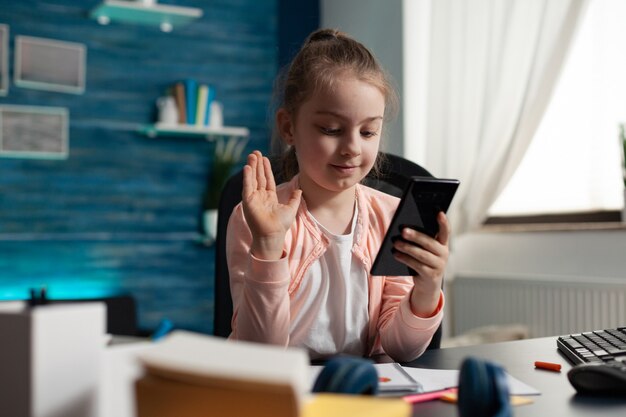 スマートフォンのビデオ通話カメラで手を振っている若い学生