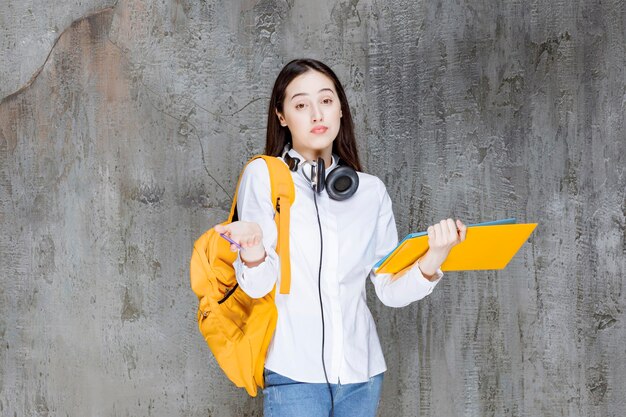 헤드폰과 책을 들고 서서 찾고 있는 젊은 학생. 고품질 사진