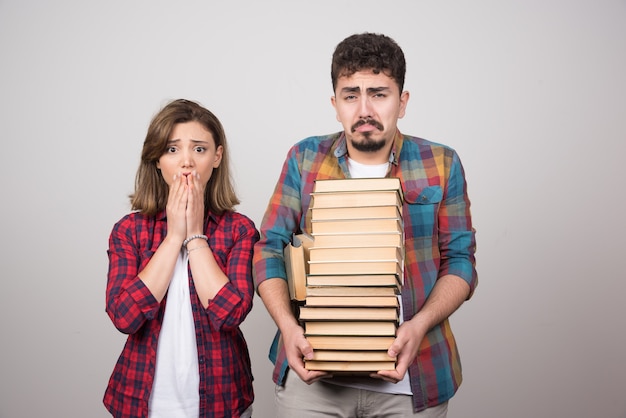 Young students looking sad and holding books on gray background.