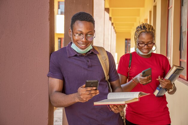 Giovani studenti che indossano maschere e tengono in mano libri e telefoni in un campus