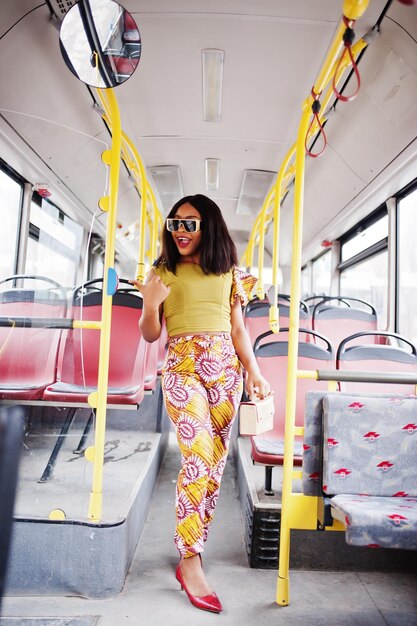 Молодая стильная афроамериканка в современных солнцезащитных очках едет на автобусе