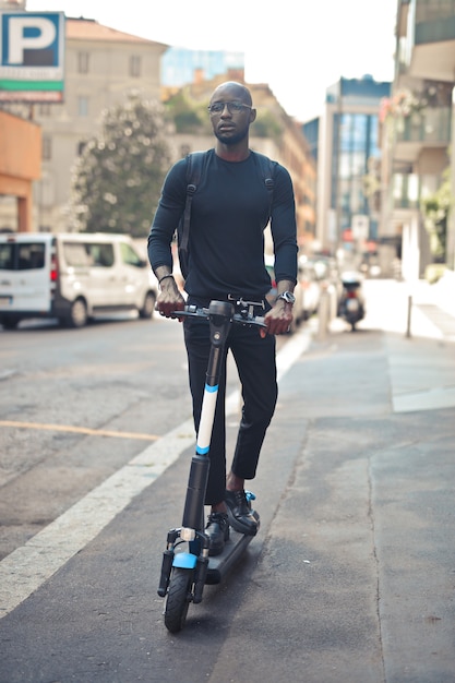 Young stylish African male with glasses riding a scooter under the sunlight at daytime