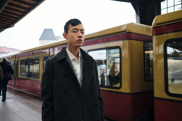 지하철 플랫폼에서 기차를 기다리는 동안 자신감 있게 카메라를 바라보는 젊고 세련된 아시아 사업가