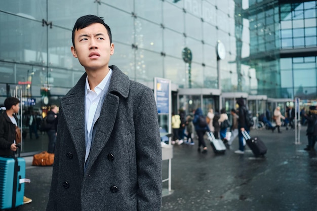 Young stylish Asian businessman thoughtfully waiting taxi on street near airport