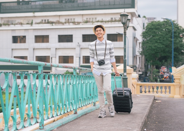 여행 가방과 카메라를 들고 여행하는 젊은 세련된 아시아 남자.