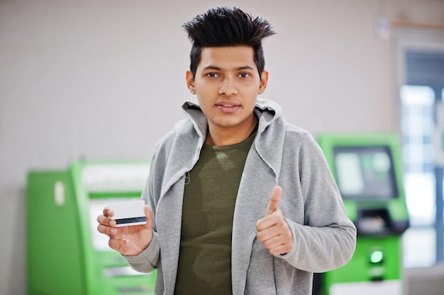 신용 카드를 손에 들고 있는 세련된 아시아 남성은 녹색 ATM에 엄지손가락을 치켜들고 있습니다.