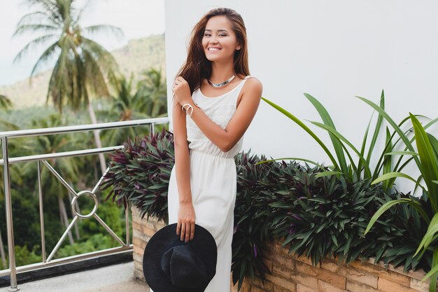 Young stylish asian woman in white boho dress, vintage style, natural, smiling, happy, tropical vacation, hotel, honey moon