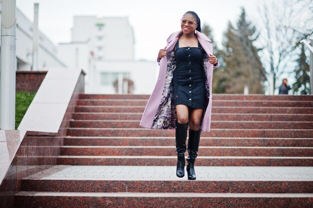 Young stylish beautiful african american woman in street against stairs wearing fashion outfit coat eyeaglasses