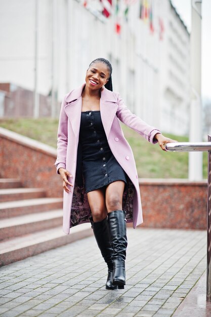 Молодая стильная красивая афроамериканка на улице в модном пальто против флагов разных стран мира