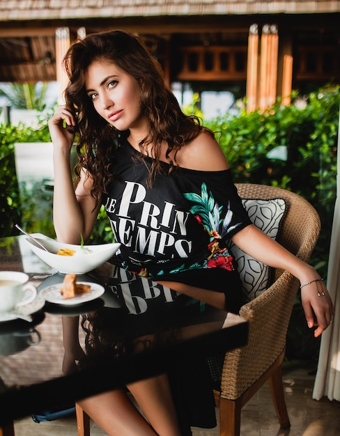 Free photo young stylish beautiful woman sitting at tropical resort cafe, smiling