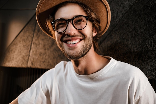 Бесплатное фото Молодой стильный жизнерадостный мужчина счастливо смотрит в камеру в современной студии звукозаписи