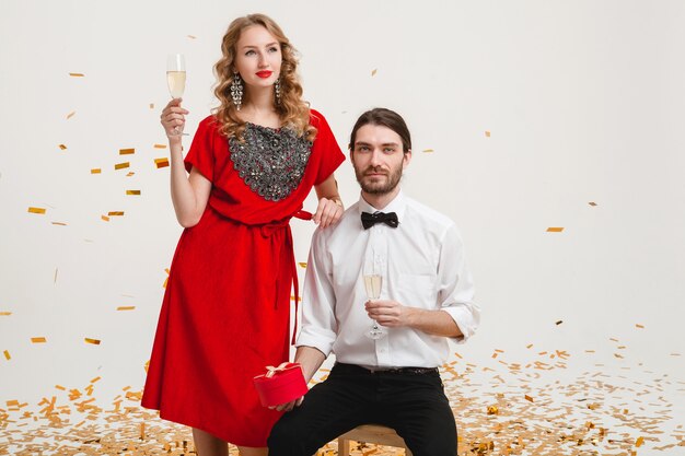 Молодая стильная влюбленная пара держит бокалы и пьет шампанское, празднуя новый год