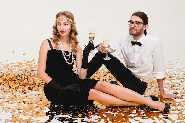 Young stylish couple in love, sitting on floor, throwing golden confetti