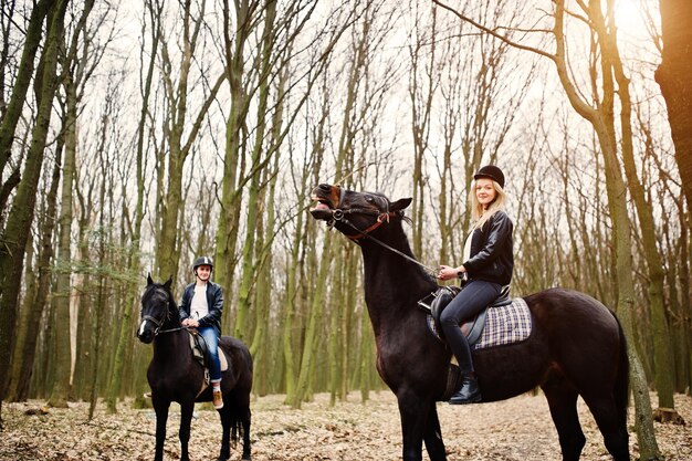 Young stylish couple riding on horses at autumn forest