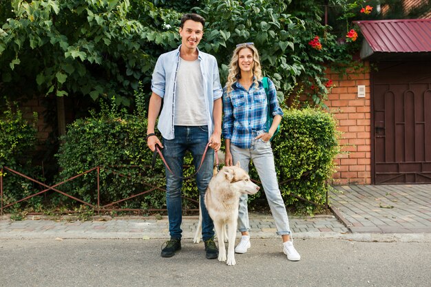 通りで犬を連れて歩いてスタイリッシュなカップル。男と女のハスキー犬と一緒に幸せ