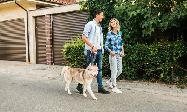 通りで犬を連れて歩いてスタイリッシュなカップル。男と女のハスキー犬と一緒に幸せ