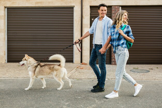 通りで犬を連れて歩いてスタイリッシュなカップル。男と女のハスキー犬と一緒に幸せ