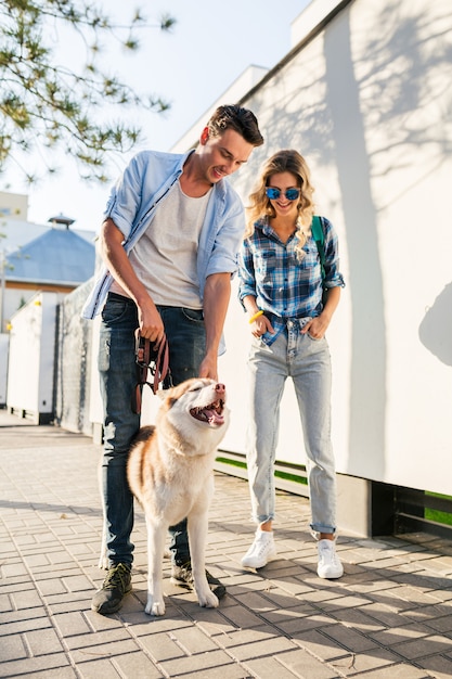 通りで犬を連れて歩いてスタイリッシュなカップル。男と女のハスキー犬と一緒に幸せ