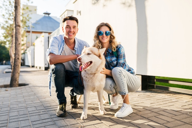 Young stylish couple walking with dog in street. man and woman happy together with husky breed,