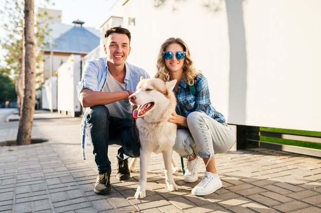 通りで犬を連れて歩いてスタイリッシュなカップル。男と女のハスキー犬と一緒に幸せ