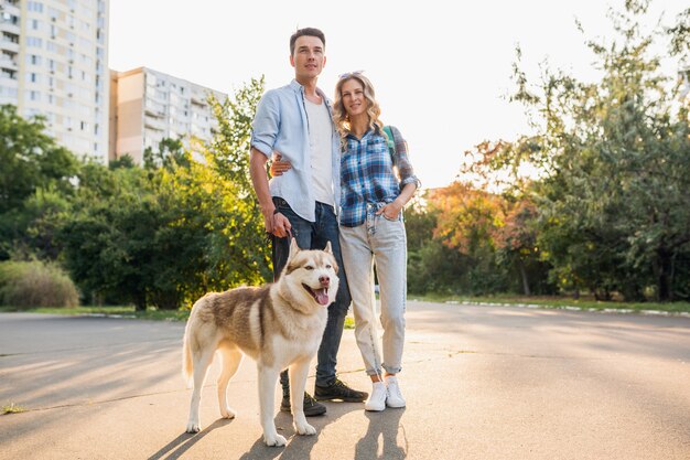 通りで犬を連れて歩いてスタイリッシュなカップル。男と女のハスキー犬と一緒に幸せ