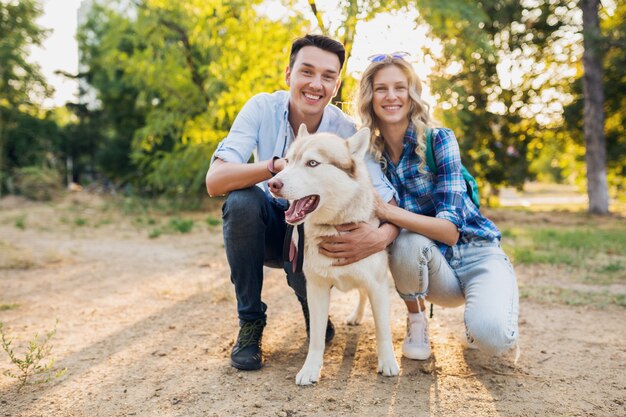 通りで犬を連れて歩いてスタイリッシュなカップル。男と女のハスキー犬と一緒に幸せ