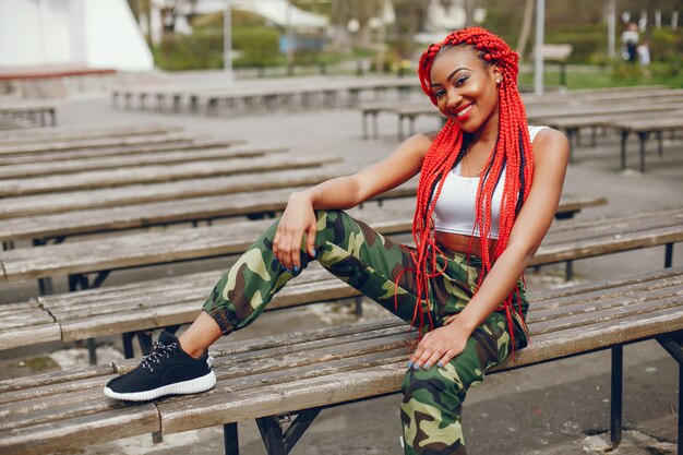 A young and stylish dark-skinned girl with red dreads sitting in the summer park