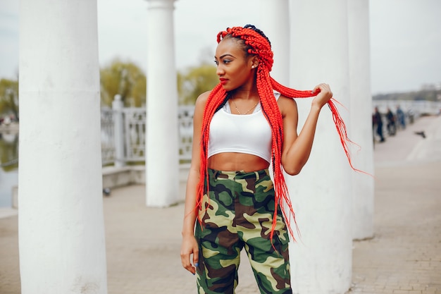 A young and stylish dark-skinned girl with red dreads walking in the summer park