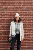 Free photo young stylish female photographer posing against brick wall in the city