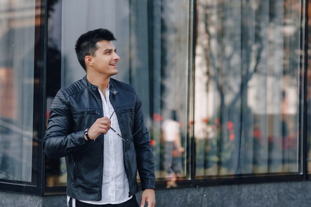 young stylish guy in glasses in black leather jacket on glass surface