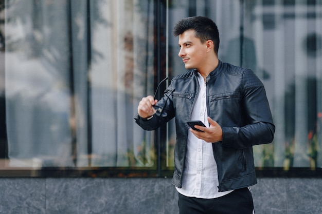 Giovane ragazzo elegante con gli occhiali in giacca di pelle nera con telefono