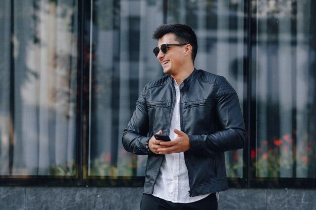 young stylish guy in glasses in black leather jacket with phone 