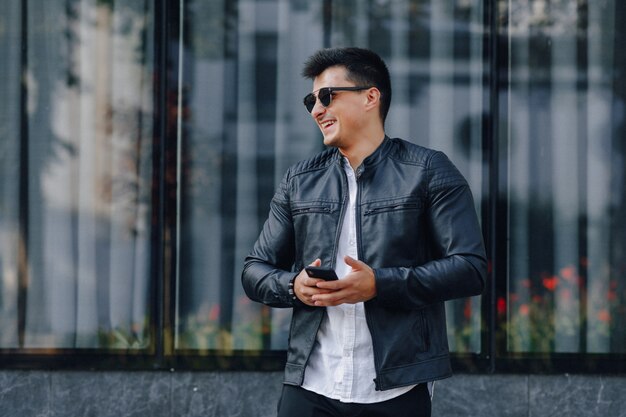 Young stylish guy in glasses in black leather jacket with phone 