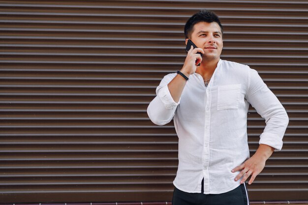 シンプルな表面に電話で話しているシャツの若いスタイリッシュな男
