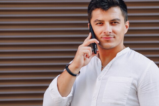 Молодой стильный парень в рубашке разговаривает по телефону на простой поверхности